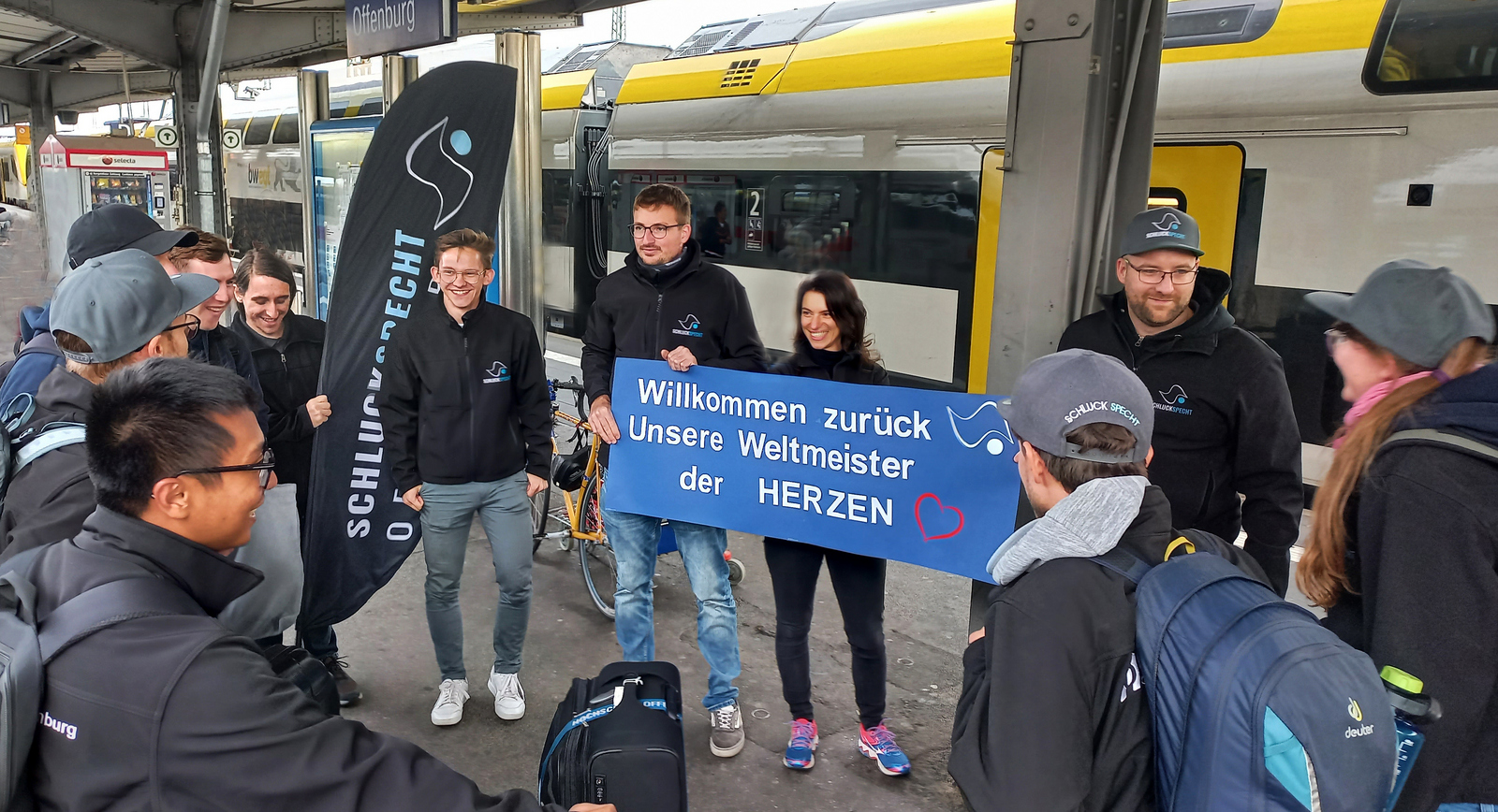 Team wird auf dem Bahnhof Offenburg von Kommilitonen mit einem Plakat Weltmeister der herzen begrüßt